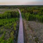Rak väg genom tät skog och kalhyggen, sedd från luften
